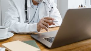 Doctor in white lab coat points at laptop screen.