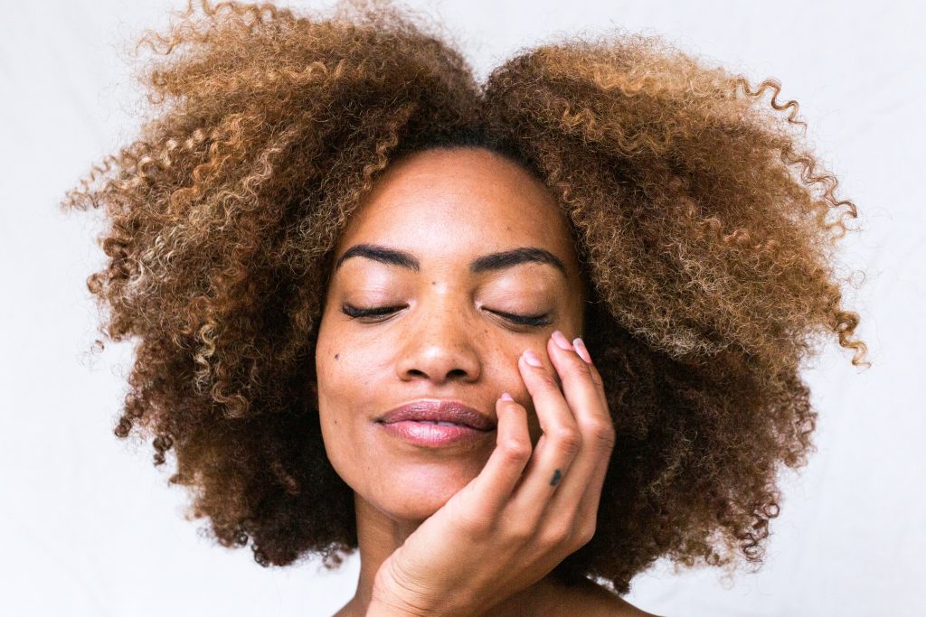 a woman with clear, wrinkle-free skin smiles with her eyes closed and her hand over her face