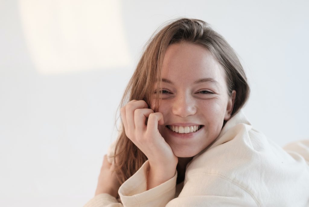 a young woman smiles with her hand pressed to her face.