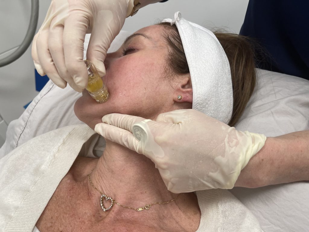 woman is laying down while getting an aquagold facials done by a cosmetic professional.