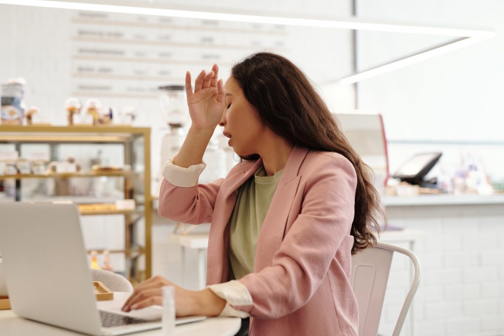 woman sneezing at a cafe table with her laptop.