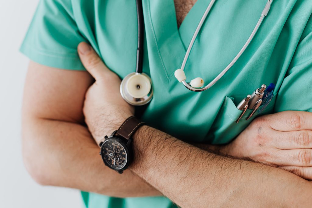 a male doctor folds his arms around his chest. He wears scrubs and medical tools.