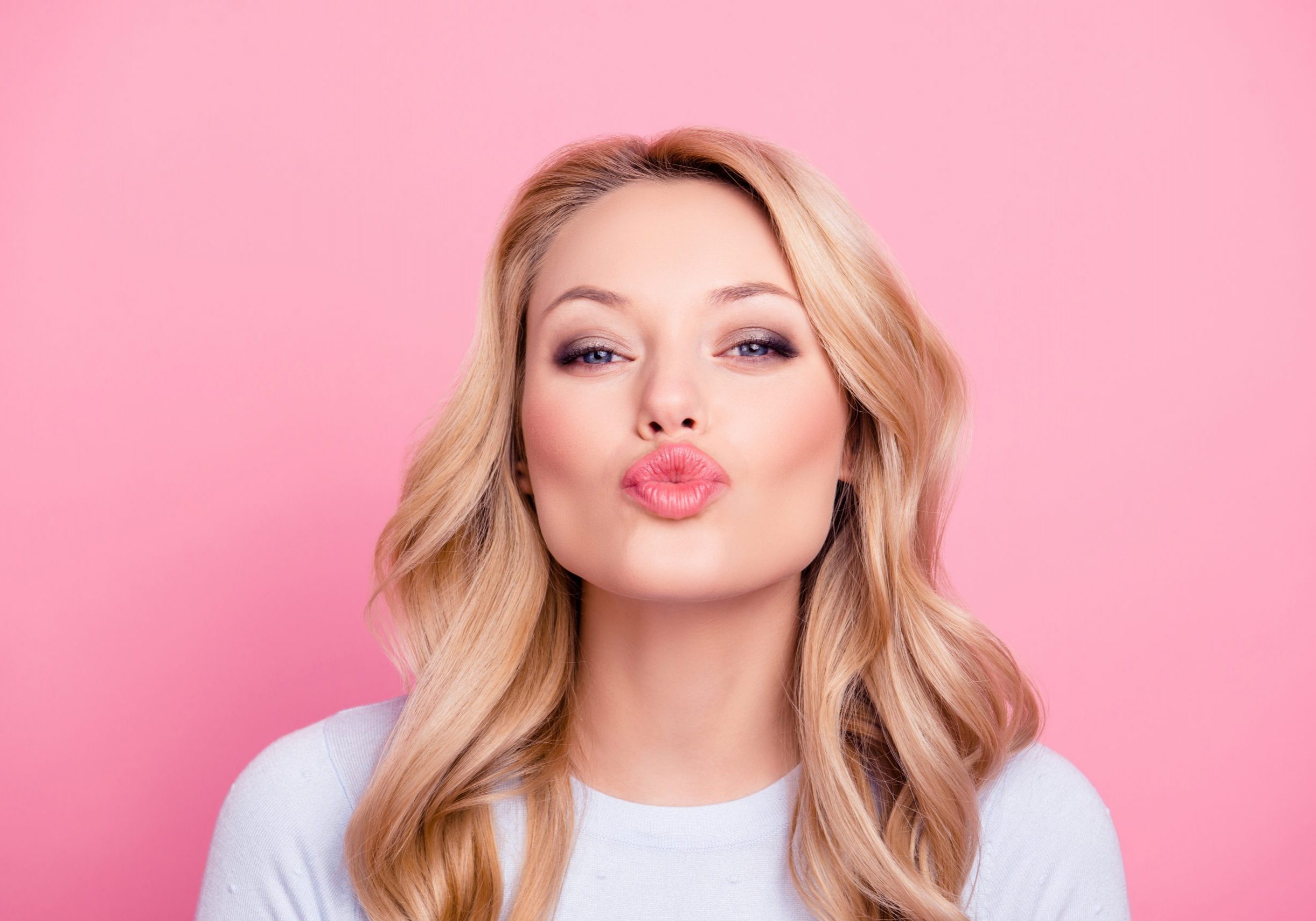 Portrait of cute lovely girl in casual outfit with modern hairdo sending blowing kiss with pout lips looking at camera isolated on pink background. Affection feelings concept